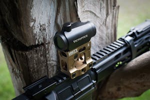 Close-up of a VictOptics gun sight mounted on a weapon outdoors with natural background.